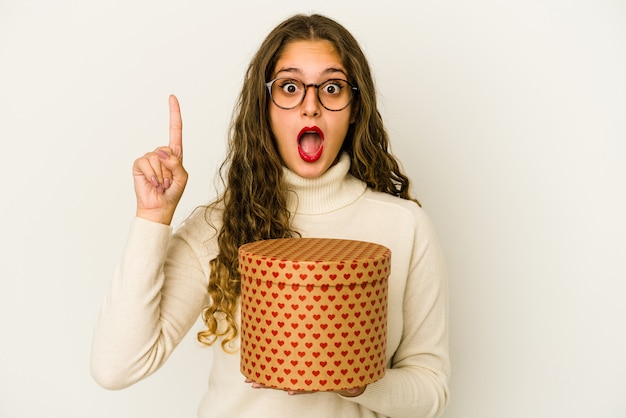 Foto jovem mulher caucasiana, segurando uma caixa de dia dos namorados de coração isolada, tendo uma ótima ideia, o conceito de criatividade.