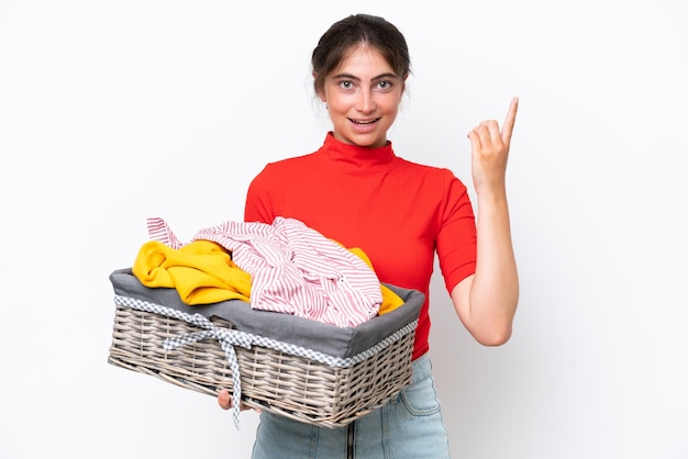 Jovem mulher caucasiana segurando uma cesta de roupas isolada em fundo branco apontando uma grande ideia