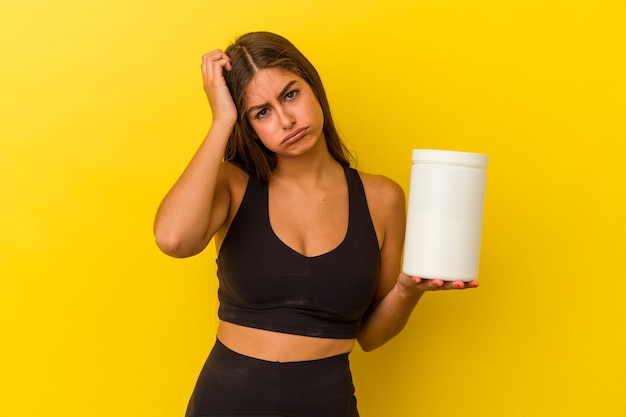 Jovem mulher caucasiana, segurando uma garrafa de proteína isolada em um fundo amarelo, sendo chocada, ela se lembrou de uma reunião importante.