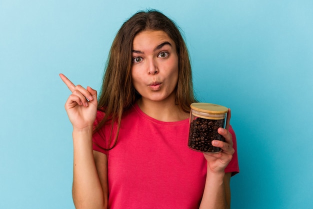 Jovem mulher caucasiana, segurando uma jarra de café isolada sobre fundo azul, tendo uma ótima ideia, o conceito de criatividade.