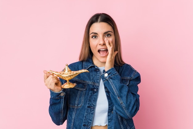 Jovem mulher caucasiana segurando uma lâmpada mágica gritando animado para a frente.