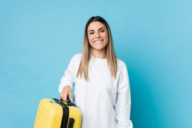 Jovem mulher caucasiana, segurando uma mala feliz, sorridente e alegre.