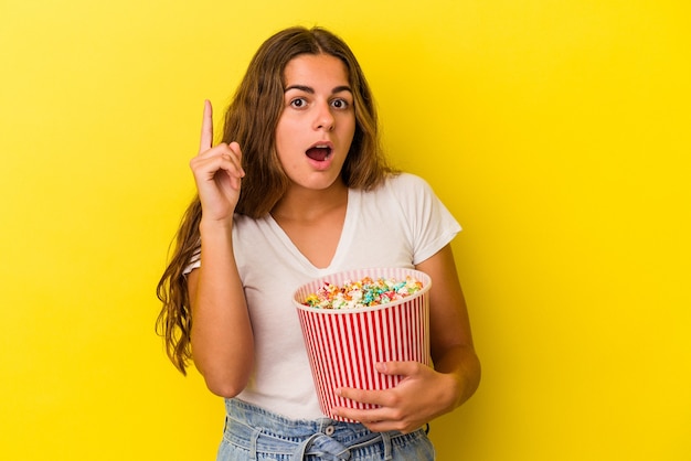 Jovem mulher caucasiana, segurando uma pipoca isolada no fundo amarelo, tendo uma ideia, o conceito de inspiração.