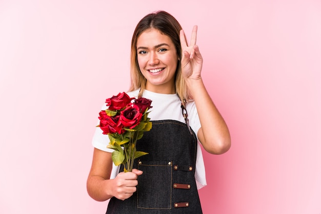 Jovem mulher caucasiana segurando uma rosas mostrando sinal de vitória e sorrindo amplamente.