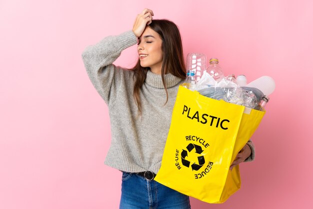 Jovem mulher caucasiana segurando uma sacola cheia de garrafas plásticas para reciclar, isolada na parede rosa, percebeu algo e pretende a solução