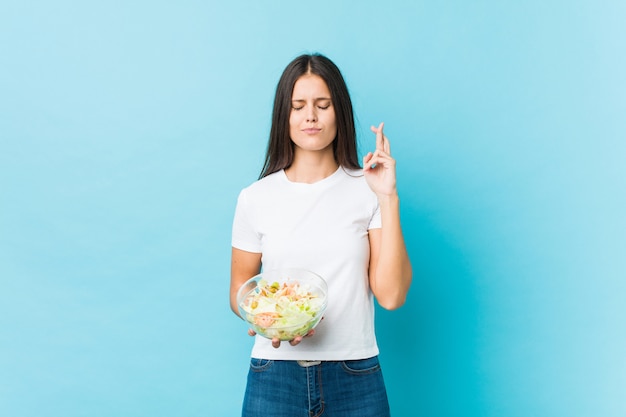 Jovem mulher caucasiana, segurando uma salada cruzando os dedos por ter sorte