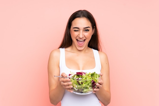 Jovem mulher caucasiana segurando uma salada isolada na parede rosa