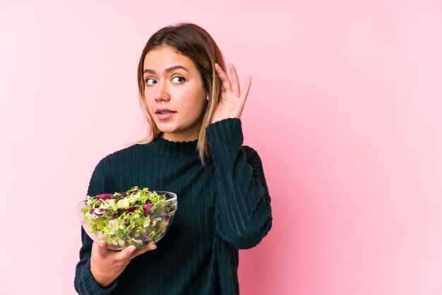 Jovem mulher caucasiana, segurando uma salada isolada, tentando ouvir uma fofoca.