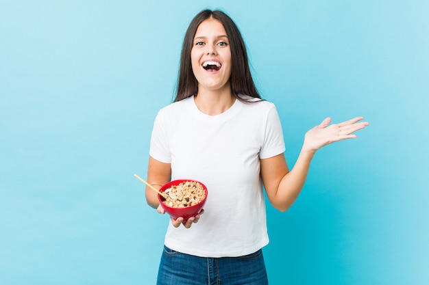 Jovem mulher caucasiana, segurando uma tigela de cereais comemorando uma vitória ou sucesso