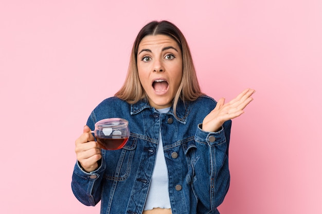 Jovem mulher caucasiana, segurando uma xícara de chá, comemorando uma vitória ou sucesso