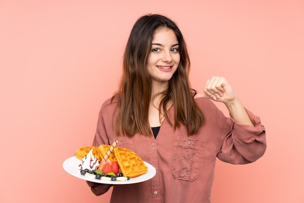 Jovem mulher caucasiana, segurando waffles isolados na parede rosa, orgulhoso e satisfeito