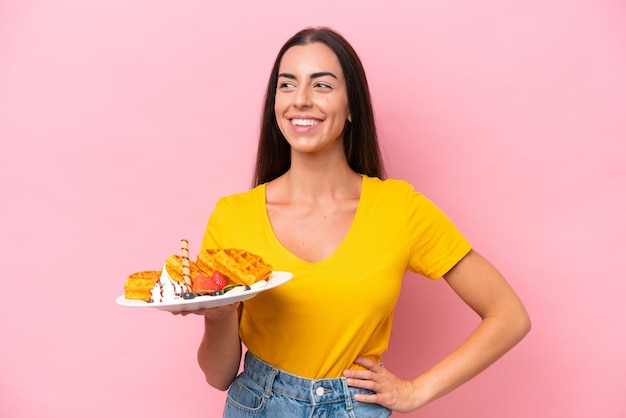 Jovem mulher caucasiana segurando waffles isolados no fundo rosa