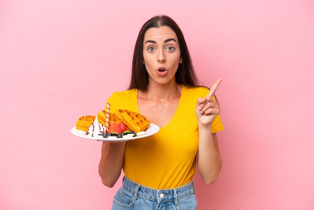 Jovem mulher caucasiana segurando waffles isolados no fundo rosa