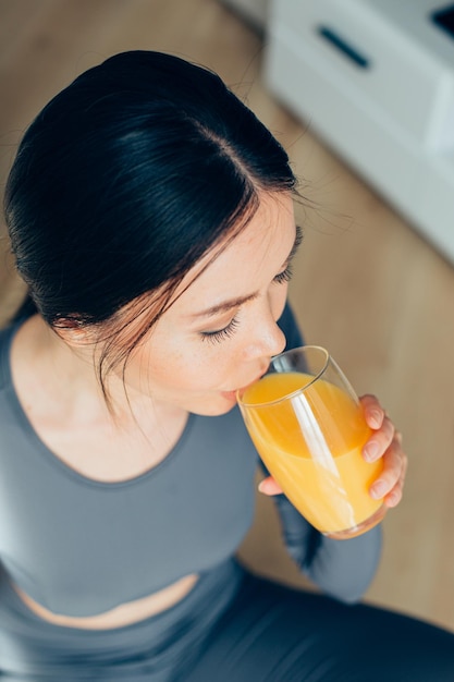 Jovem mulher caucasiana sentada no chão e bebendo suco de laranja do copo