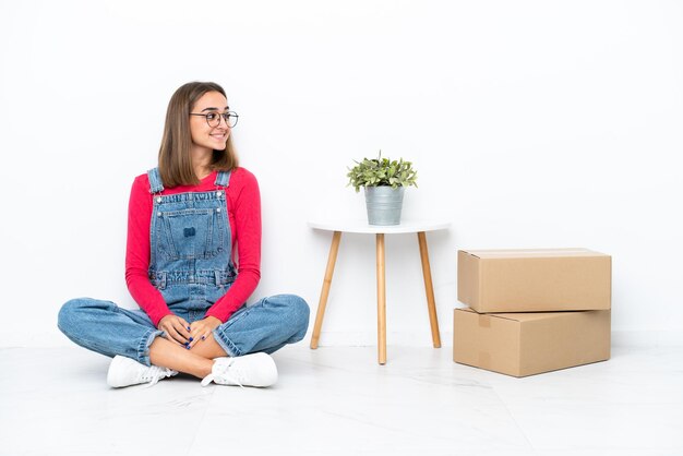 Jovem mulher caucasiana sentada no chão entre caixas olhando de lado