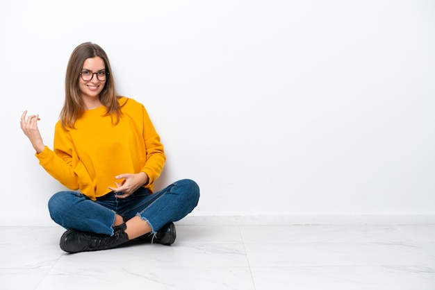 Foto jovem mulher caucasiana sentada no chão, isolada no fundo branco, fazendo gesto de guitarra