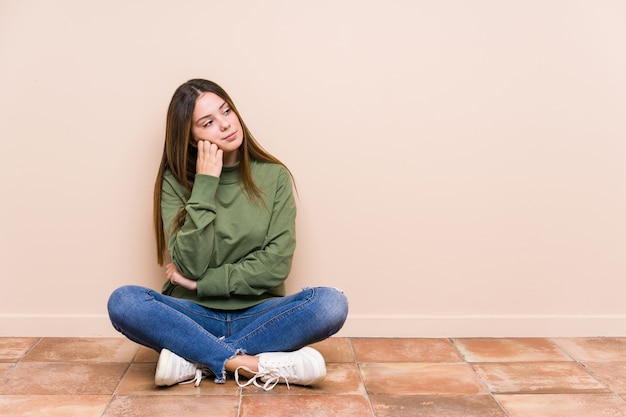 Jovem mulher caucasiana, sentada no chão que se sente triste e pensativa, olhando para o espaço em branco.