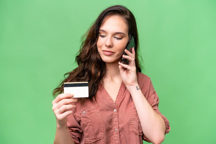 Foto jovem mulher caucasiana sobre fundo isolado comprando com o celular com um cartão de crédito