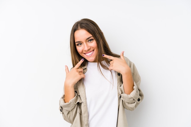 Foto jovem mulher caucasiana sorri, apontando os dedos na boca.