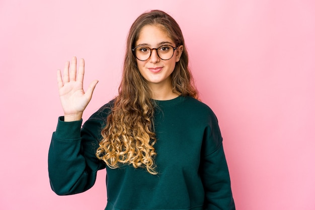 Jovem mulher caucasiana, sorrindo alegre mostrando o número cinco com os dedos.