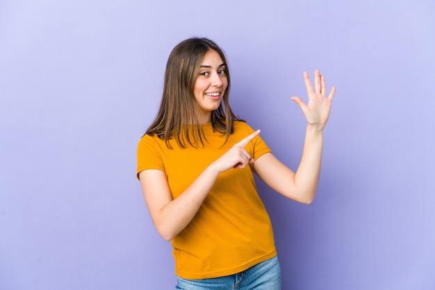 Jovem mulher caucasiana, sorrindo alegre mostrando o número cinco com os dedos.