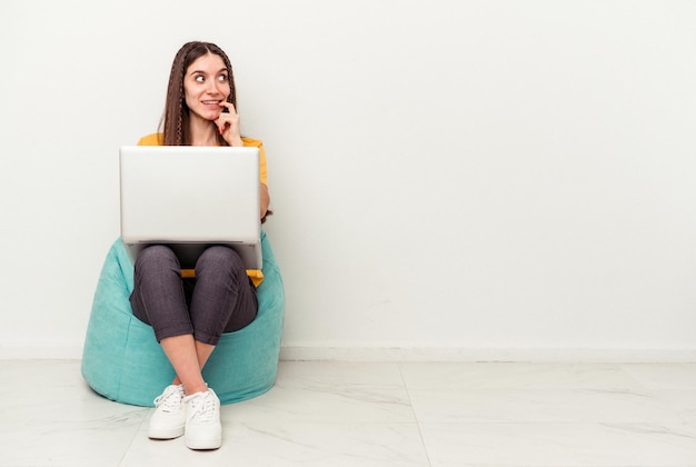 Jovem mulher caucasiana trabalhando com laptop sentado em um sopro isolado no fundo branco relaxado pensando em algo olhando para um espaço de cópia.