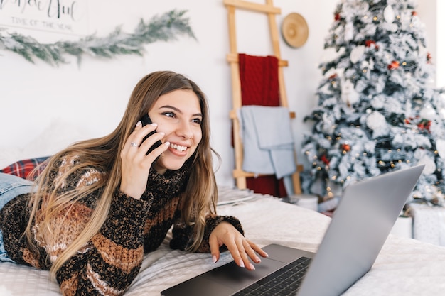 Jovem mulher caucasiana usando celular e laptop, conversando com amigos nas férias