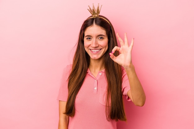 Jovem mulher caucasiana usando coroa isolada em fundo rosa alegre e confiante, mostrando um gesto de ok.