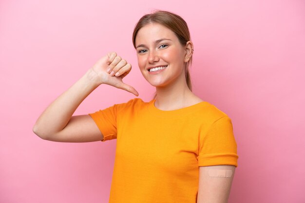 Jovem mulher caucasiana usando curativo isolado em fundo rosa orgulhoso e satisfeito