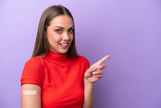 Jovem mulher caucasiana usando curativo isolado no fundo roxo surpreso e apontando o dedo para o lado