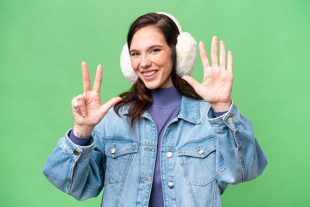 Jovem mulher caucasiana usando muffs de inverno sobre fundo isolado contando oito com os dedos