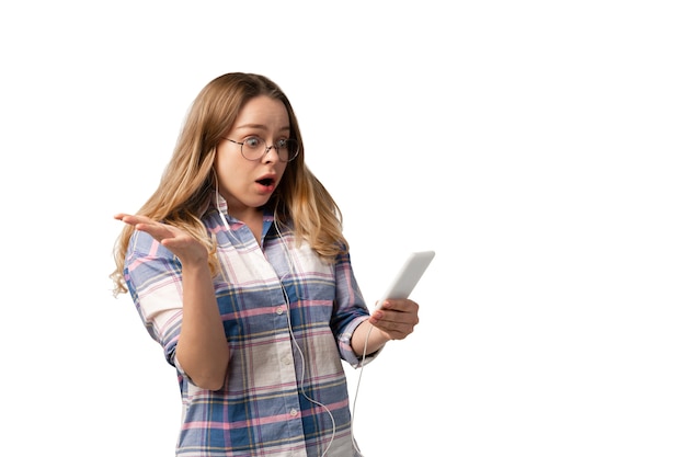 Jovem mulher caucasiana, usando smartphone, dispositivos, gadgets isolados na parede branca do estúdio.