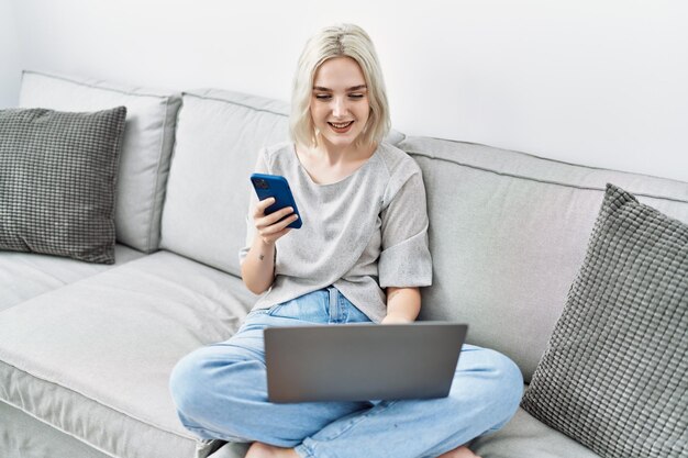 Jovem mulher caucasiana usando smartphone e laptop em casa