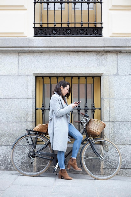 Jovem mulher caucasiana usando telefone celular ao ar livre Ela está ao lado de uma bicicleta clássica de turismo