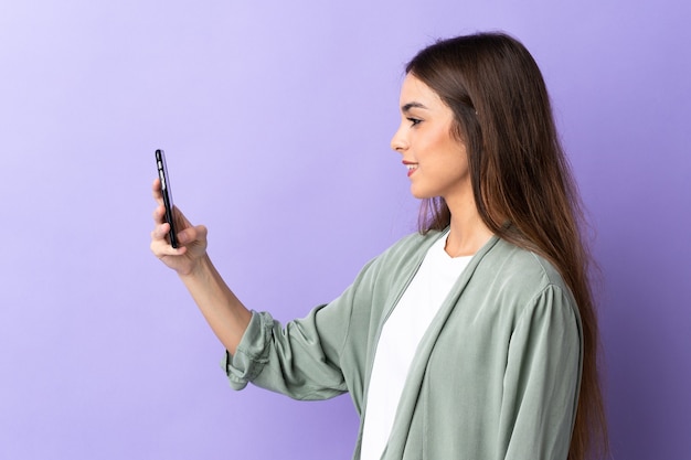 Jovem mulher caucasiana usando telefone celular roxo com expressão feliz