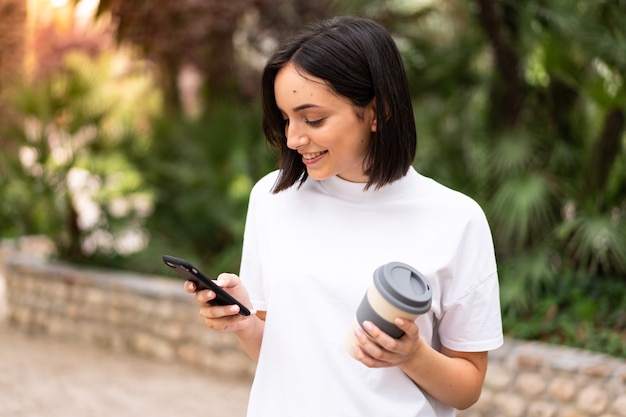 Jovem mulher caucasiana usando um telefone ao ar livre