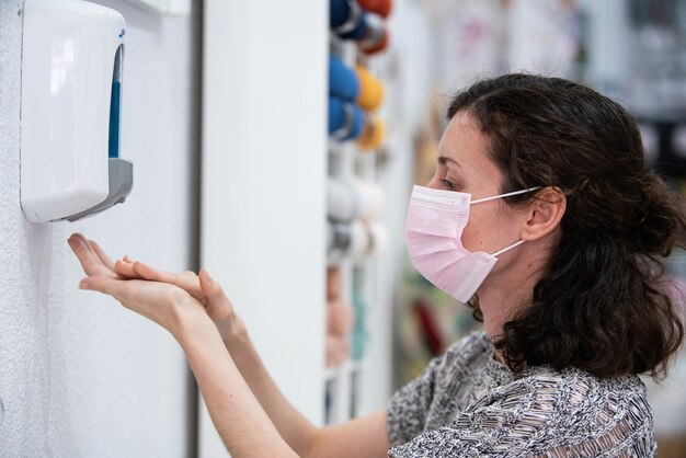 Jovem mulher caucasiana usando uma máscara facial higiênica e usando gel desinfetante para limpar as mãos