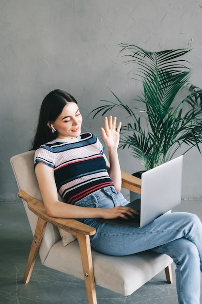 Jovem mulher caucasiana, usando videochamada no laptop, tecelagem.