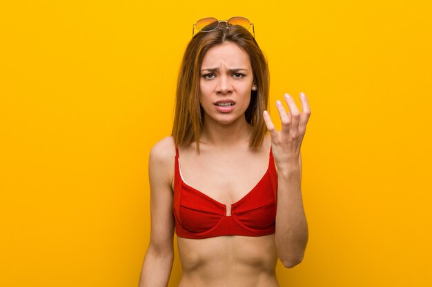 Jovem mulher caucasiana, vestindo biquíni e óculos de sol, gritando de raiva.