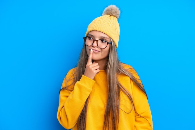 Jovem mulher caucasiana vestindo roupas de inverno isoladas em fundo azul com dúvidas ao olhar para cima