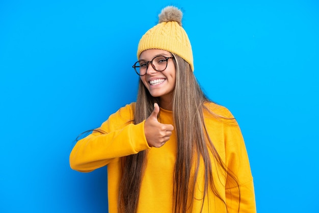 Jovem mulher caucasiana vestindo roupas de inverno isoladas em fundo azul, dando um polegar para cima gesto