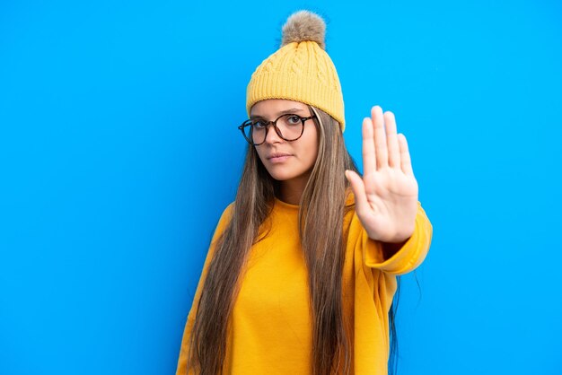 Jovem mulher caucasiana vestindo roupas de inverno isoladas em fundo azul fazendo gesto de parada