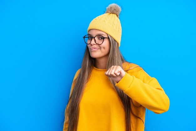 Jovem mulher caucasiana vestindo roupas de inverno isoladas em fundo azul orgulhosa e satisfeita