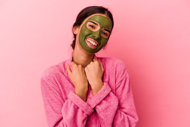 Jovem mulher caucasiana vestindo um roupão de banho e máscara facial isolada em um fundo rosa