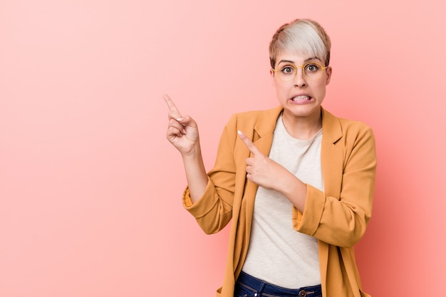 Jovem mulher caucasiana, vestindo uma roupa casual negócios chocou apontando com o dedo indicador para um espaço de cópia.