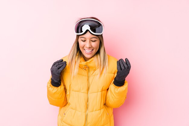 Jovem mulher caucasiana vestindo uma roupa de esqui em um fundo rosa alegre rindo muito. Conceito de felicidade.