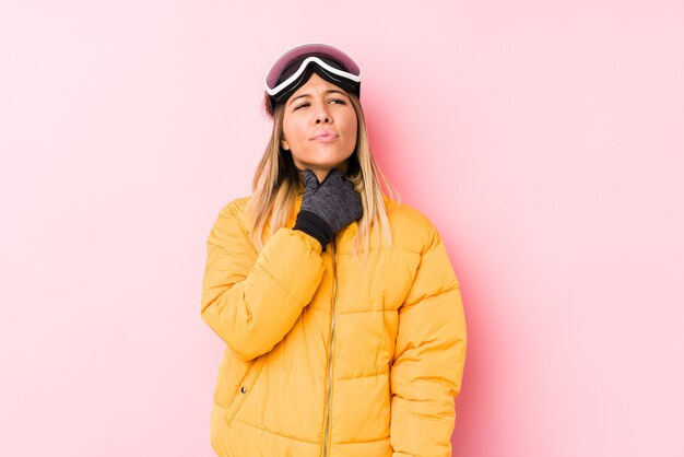 Jovem mulher caucasiana, vestindo uma roupa de esqui rosa, sofre de dor na garganta devido a um vírus ou infecção.