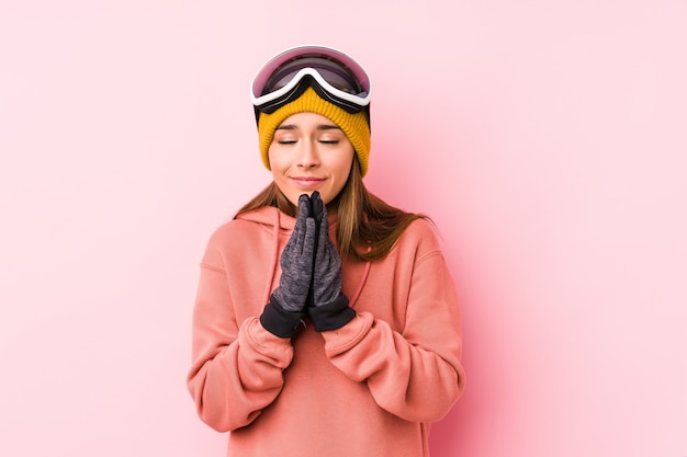 Jovem mulher caucasiana, vestindo uma roupa de esqui, segurando as mãos em rezar perto da boca, sente-se confiante.