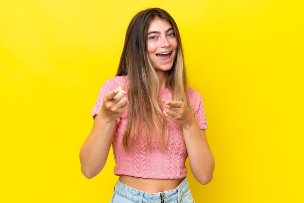 Jovem mulher caucásica isolada em fundo amarelo surpreendida e apontando para a frente