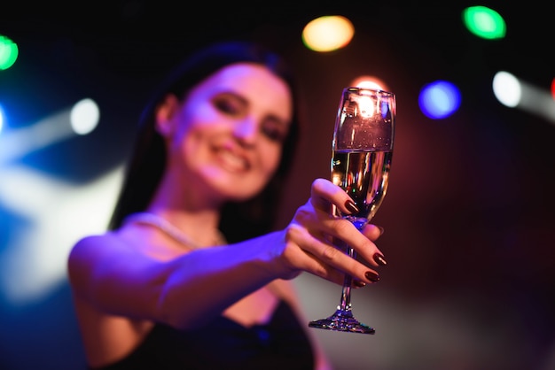 Jovem mulher celebrando vestido preto, segurando uma taça de champanhe. Festa.